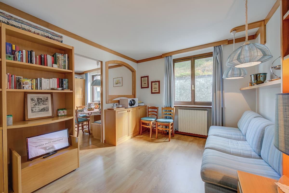 A cozy living room with a sofa, a dining table, chairs, a bookshelf, a television, and a window with curtains.