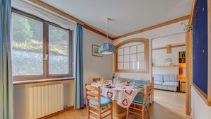 A dining area with a table set for two, a radiator, and a view of greenery outside. - Appartamento Alpetta 37 Ski In - Ski Out (Sestriere)