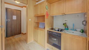 A compact kitchen with wooden cabinets, a built-in oven, and a sink with a blue faucet. - Appartamento Alpetta 37 Ski In - Ski Out (Sestriere)