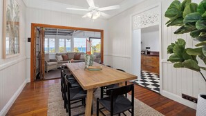 A dining area with a wooden table, black chairs, a ceiling fan, and a view through an open door. - Pacific Terrace Beach House (Coolum Beach)