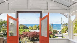 A covered porch with a view of the ocean and a red door. - Pacific Terrace Beach House (Coolum Beach)