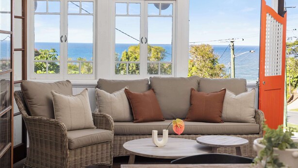 A wicker sofa with cushions, a white vase with a flower, and a round table. - Pacific Terrace Beach House (Coolum Beach)