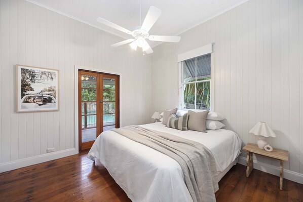 A bedroom with a bed, a ceiling fan, a window, a door, and a framed picture on the wall. - Pacific Terrace Beach House (Coolum Beach)