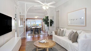 A living room with a white sofa, a round wooden coffee table, a flat-screen TV, and a ceiling fan. - Pacific Terrace Beach House (Coolum Beach)