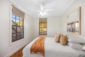 Un dormitorio con cama, ventilador de techo, ventana con vistas y un cuadro en la pared.