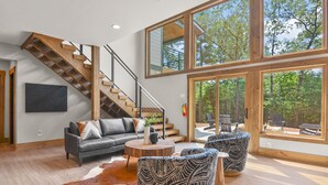 A spacious living area with a staircase, large windows, and a view of the outdoors. - Starlight Ridge ~ Indoor Pool ~ Hot Tub ~ Fire Pit ~ Fun For All! (Ellijay)
