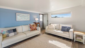 A modern living room with two white leather sofas, a beige rug, and a small wooden side table.