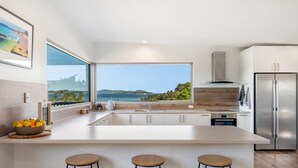 A modern kitchen with a large island, stainless steel appliances, and a view of the sea.