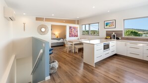 A modern kitchen with a large island, wooden flooring, and a view of the outdoors.