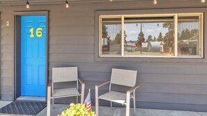 A building with a blue door marked '16', two chairs outside, and a window reflecting the outside. - Cozy 2 Bedroom Suite at Lazy Duck Inn, just 1 minute from Yellowstone! Lazy Duck 16 (West Yellowstone)