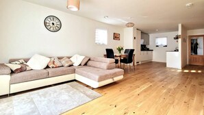 A modern living room with a sectional sofa, a dining table with chairs, and a kitchen area in the background. - Luxury 3-bed House in the Scottish Highlands (Inverness)