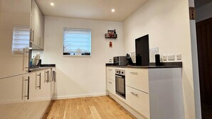 A compact kitchen with white cabinetry, a built-in oven, and a window with blinds. - Luxury 3-bed House in the Scottish Highlands (Inverness)