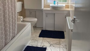 Un baño con inodoro, lavamanos y bañera. Hay una ventana sobre el lavamanos y una cortina de ducha con un diseño geométrico.