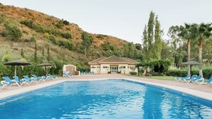 Une piscine entourée de chaises longues et de parasols, avec une végétation luxuriante et une colline en arrière-plan.