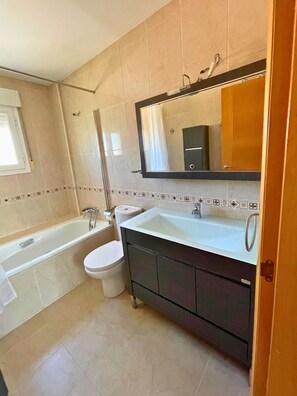 Bathroom features a bathtub, toilet, and sink, with a large mirror above the sink and a window.