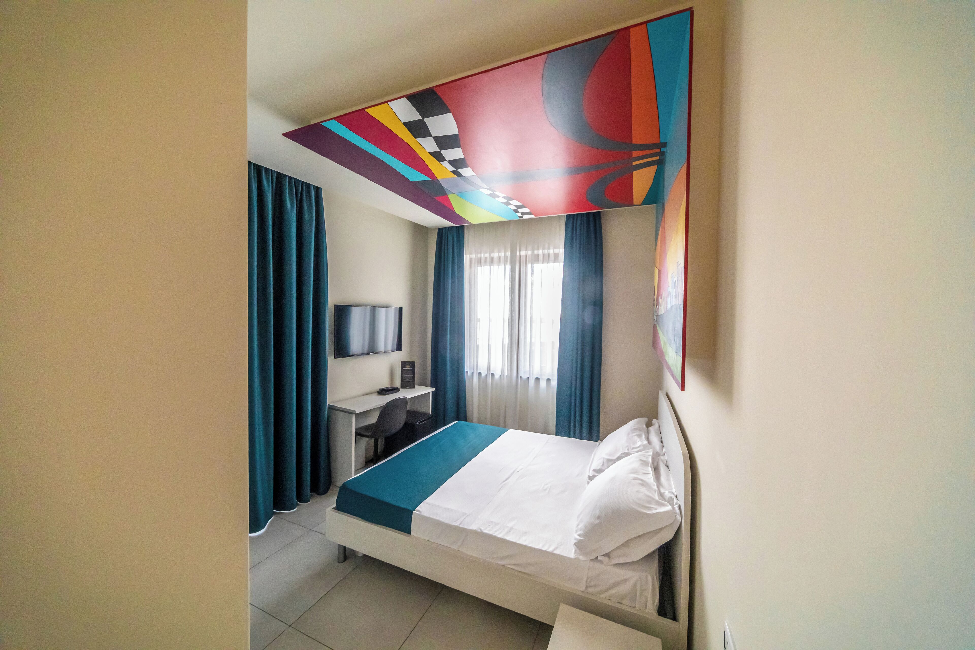 A hotel room with a bed, a desk, a chair, a television, and a window with curtains.