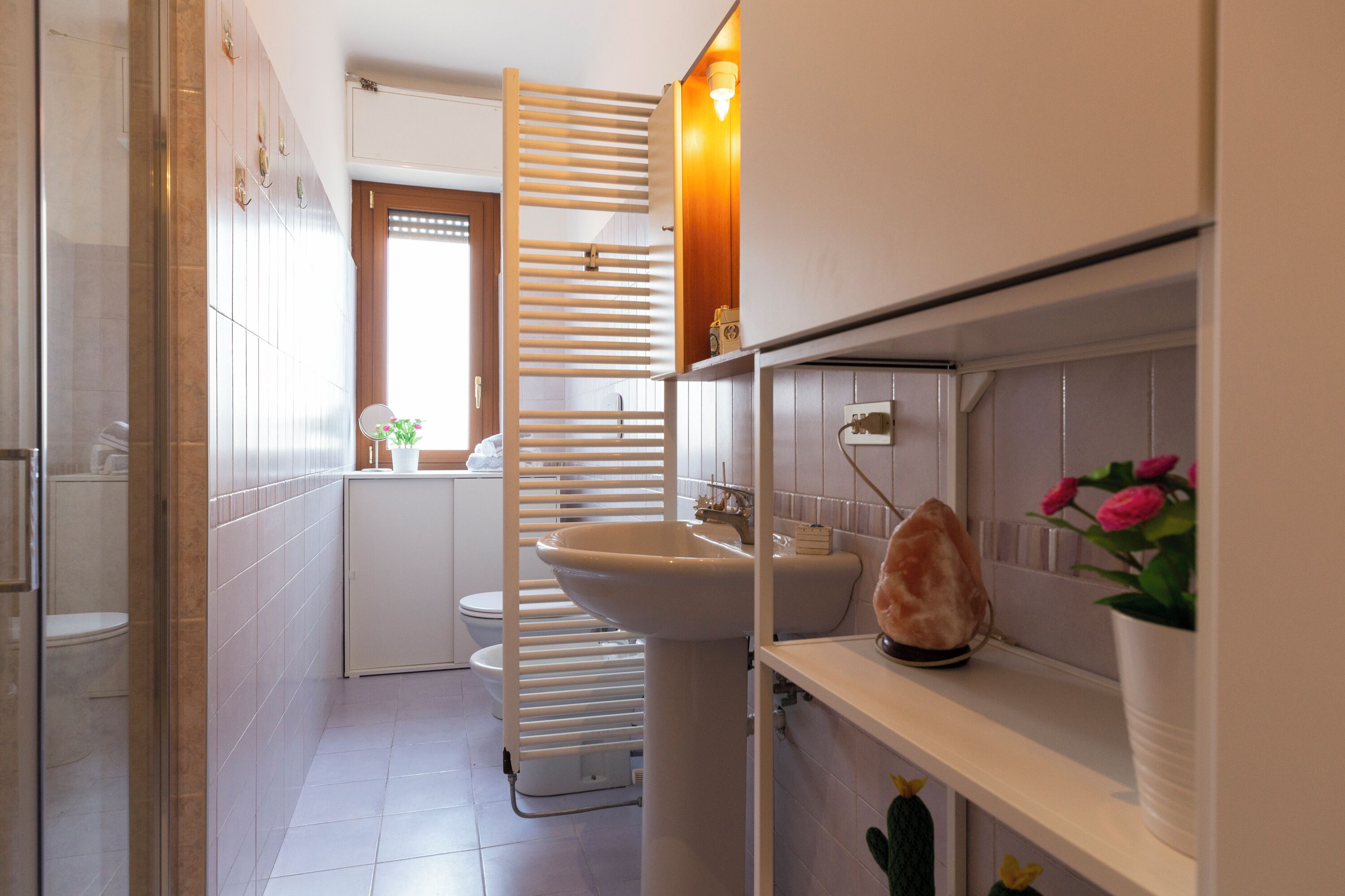 A modern bathroom with a white sink, a glass shower enclosure, and a wooden towel rack.