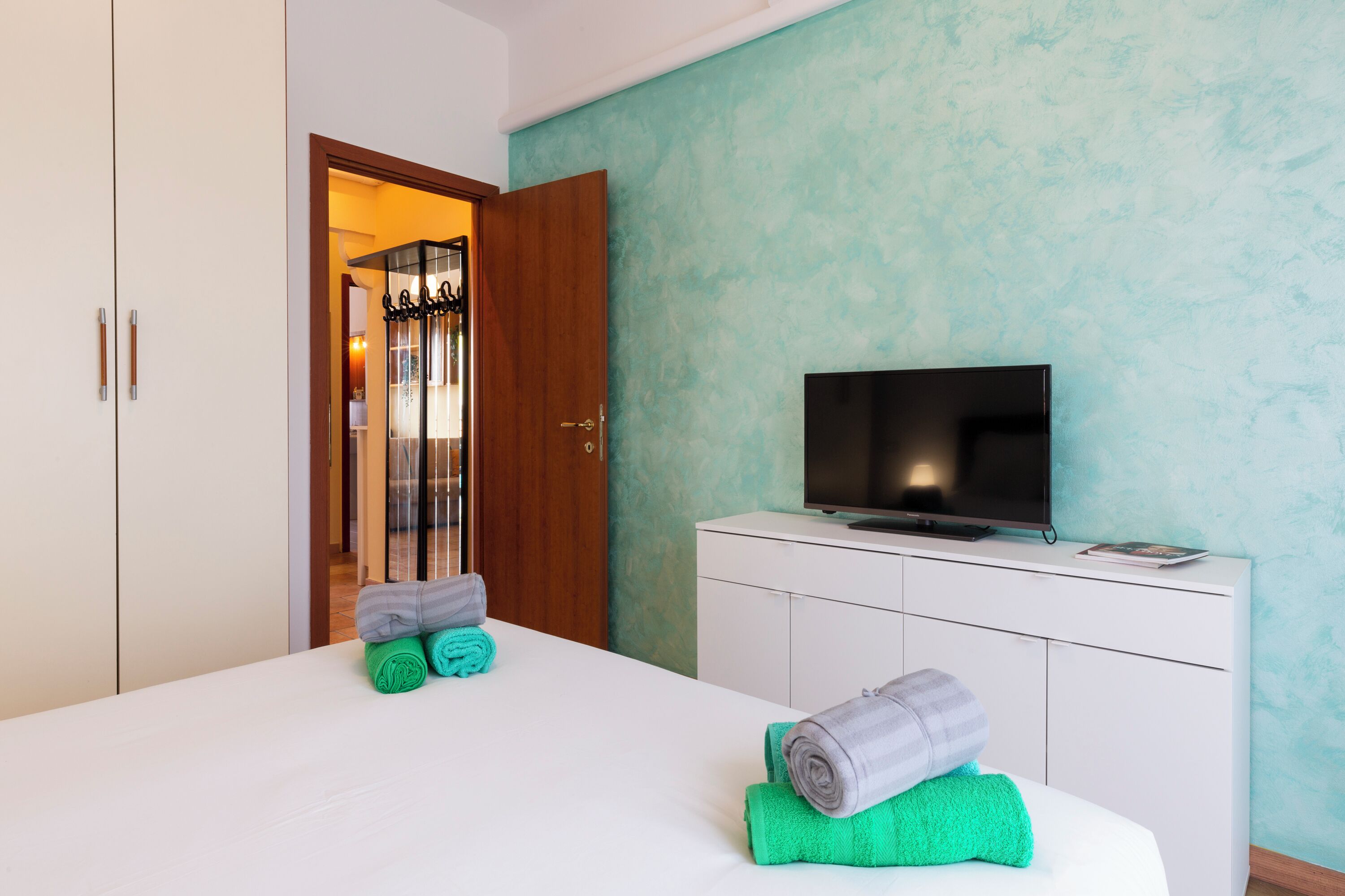 A hotel room with a bed, a television, a wardrobe, and a door leading to a bathroom.