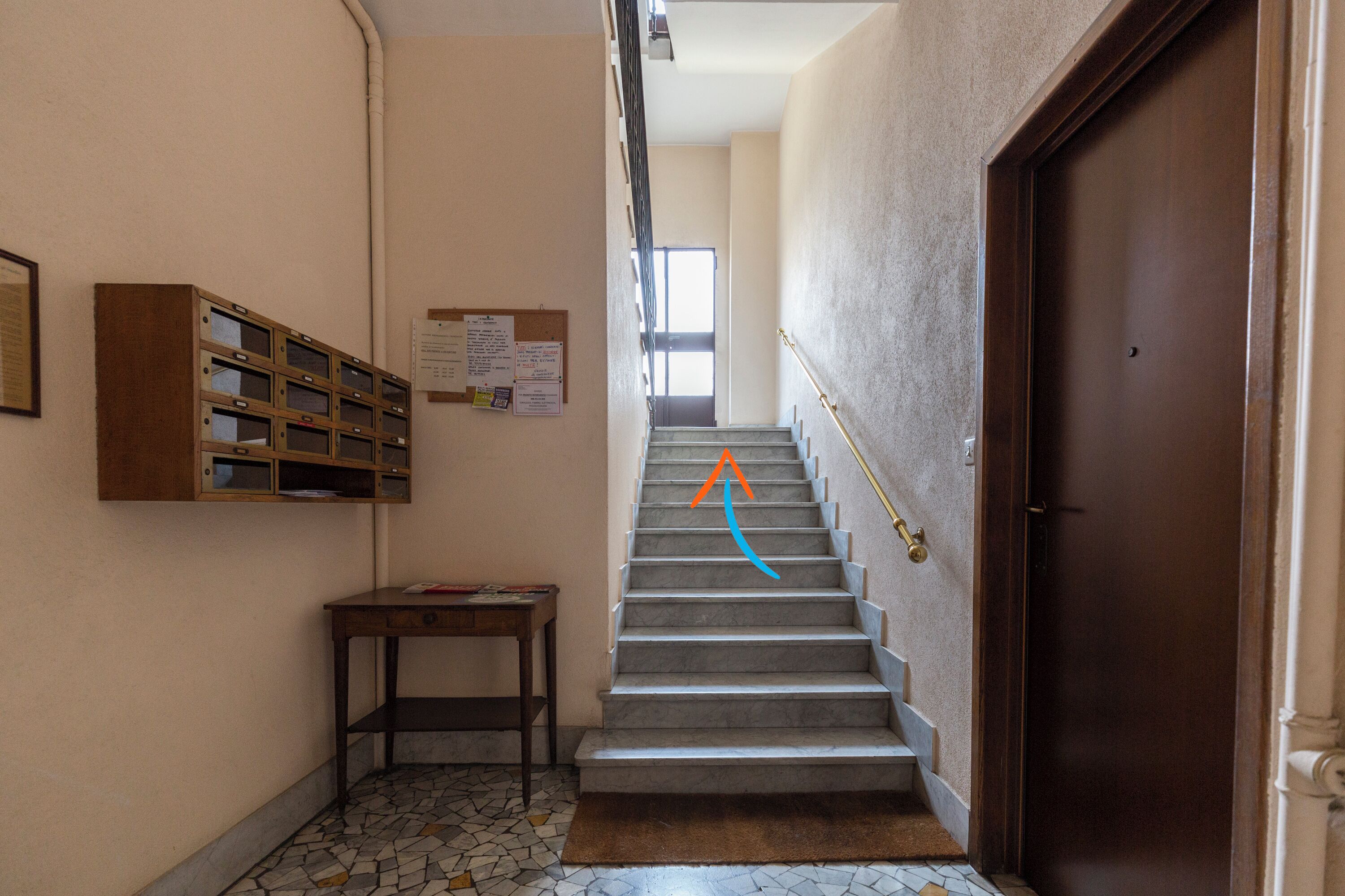 A staircase with a wooden door at the top, a bulletin board with notices, and a small table with a book.