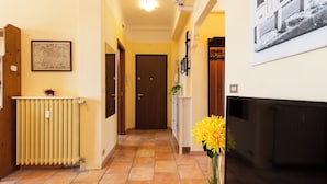Un pasillo con un radiador, una puerta, un cuadro en la pared y un jarrón con flores.
