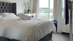 A modern hotel room with a large bed, a flat-screen TV, and a view of the city through large windows. - Stunning 1-bed Apartment in Dartford (Dartford)
