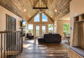 A spacious living area with a high ceiling, wooden beams, a fireplace, and a view of the outdoors. - Broadview, River, Golf Course, Games, free Attraction Tickets, WIFI!!! (Kodak)