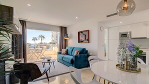 Uma sala de estar moderna com um sofá azul, cadeiras brancas, uma mesa de jantar e uma varanda com vista para palmeiras.
