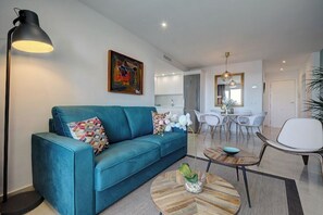 A modern living room with a teal sofa, a coffee table, and a floor lamp. There is a dining area with white chairs and a table in the background. - Apartment 'front Line Beach 2 Bedr' With Sea View, Wi-fi and Air Conditioning (Marbella)