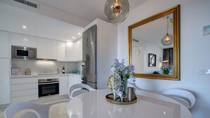 Cozinha moderna com armários brancos, eletrodomésticos de aço inoxidável e uma sala de jantar com mesa e cadeiras brancas.