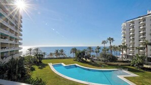 Uma piscina com borda curva, rodeada por palmeiras e vista para o oceano.