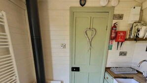 A cozy kitchen with a wood-burning stove, a green door, and a sink. - Apple hut, romantic shepherd hut retreat with log burner, hot tub, pet friendly! (Paignton)