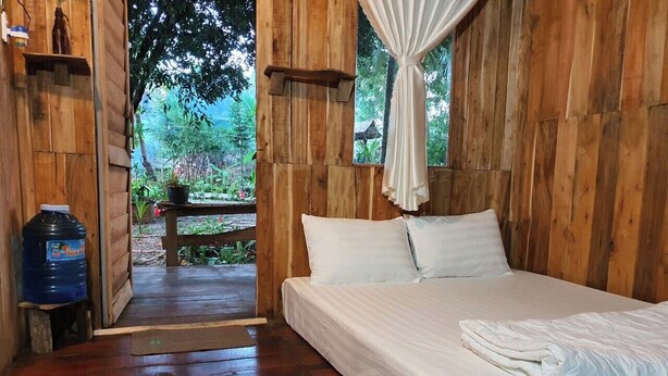 A wooden room with a bed, a water dispenser, and a view of greenery outside. - Homestay Sunny Huynh (Phu Quoc)