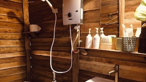 A wooden cabin bathroom with a white sink, a toilet, and a shower unit. - Homestay Sunny Huynh (Phu Quoc)