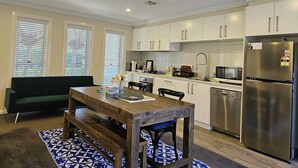 A modern kitchen with white cabinets, a stainless steel refrigerator, and a dining area with a wooden table and bench. - Modern 2BR/1BA/2+CAR Home in Central Canberra (Campbell)