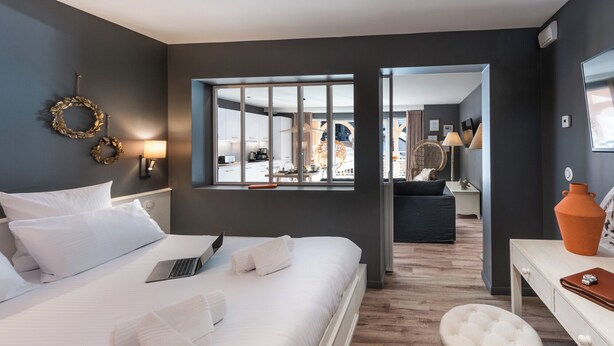 A modern hotel room with a large bed, a desk, and a view of the dining area.