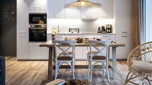 A modern kitchen with white cabinetry, a built-in oven, and a dining area with two white chairs.