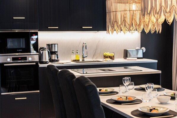 Une cuisine moderne avec un coin repas, comprenant un four à micro-ondes Bosch, une machine à café et une table à manger agrémentée d’assiettes et de verres.