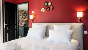 Hotellihuone, jossa on suuri sänky, valkoiset vuodevaatteet, kaksi seinälle kiinnitettyä lamppua ja peili, joka heijastaa kukkatapetoitua seinää.