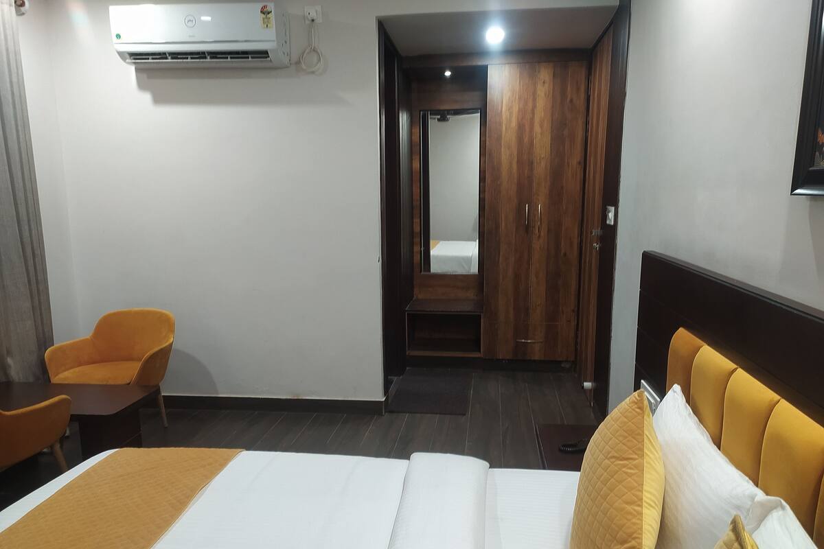 Een hotelkamer met een bed, een houten garderobe, een oranje stoel en een wandairconditioner.
