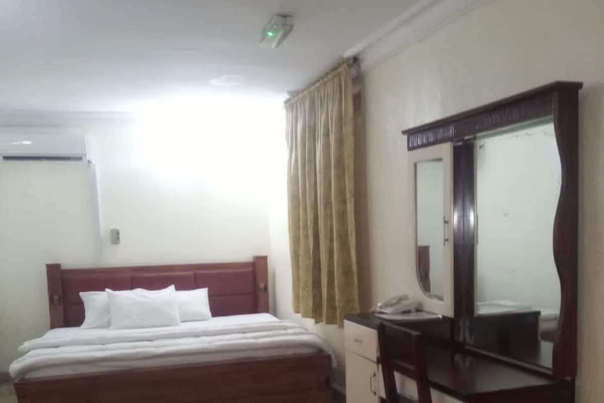 Habitación de hotel con cama, escritorio, silla, espejo y ventana con cortinas.