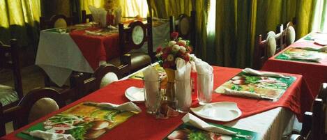 A dining area with tables set for meals, featuring red tablecloths and placemats with food illustrations.