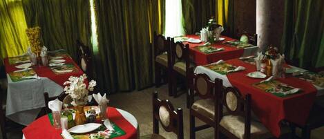 A dining area with multiple tables set for meals, each with a red tablecloth and white plates.