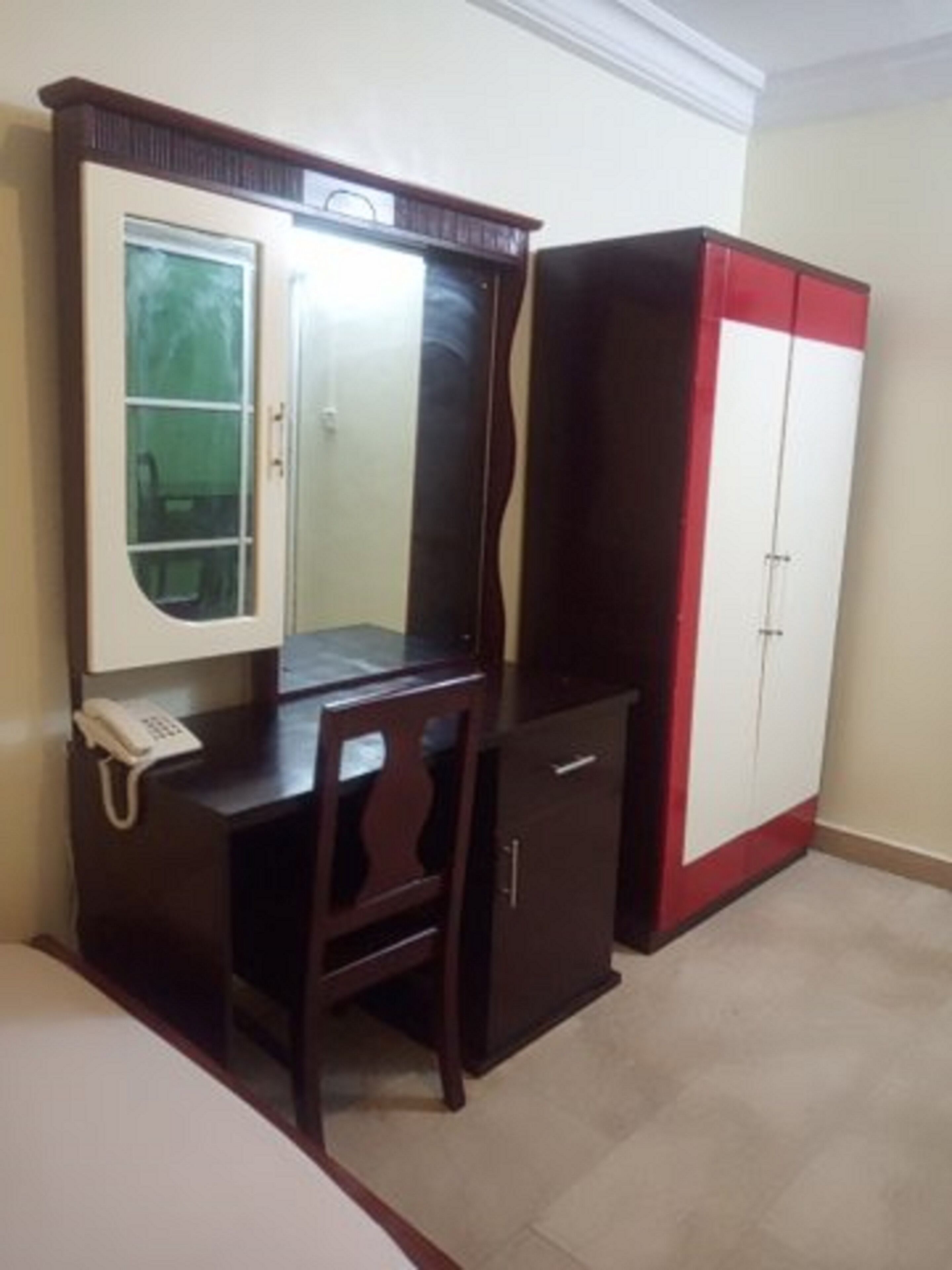 A room with a wooden desk, a chair, a telephone, and a wardrobe with a red and white design.