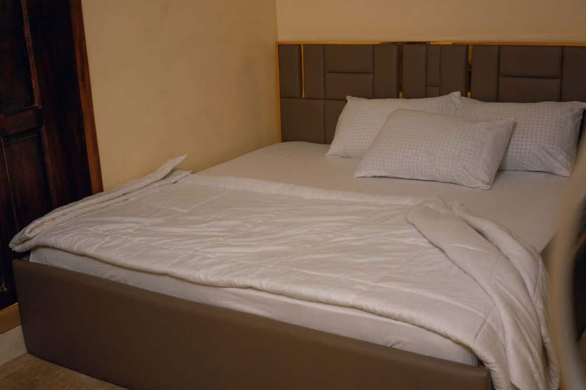 Una cama con cabecera, almohadas y manta.