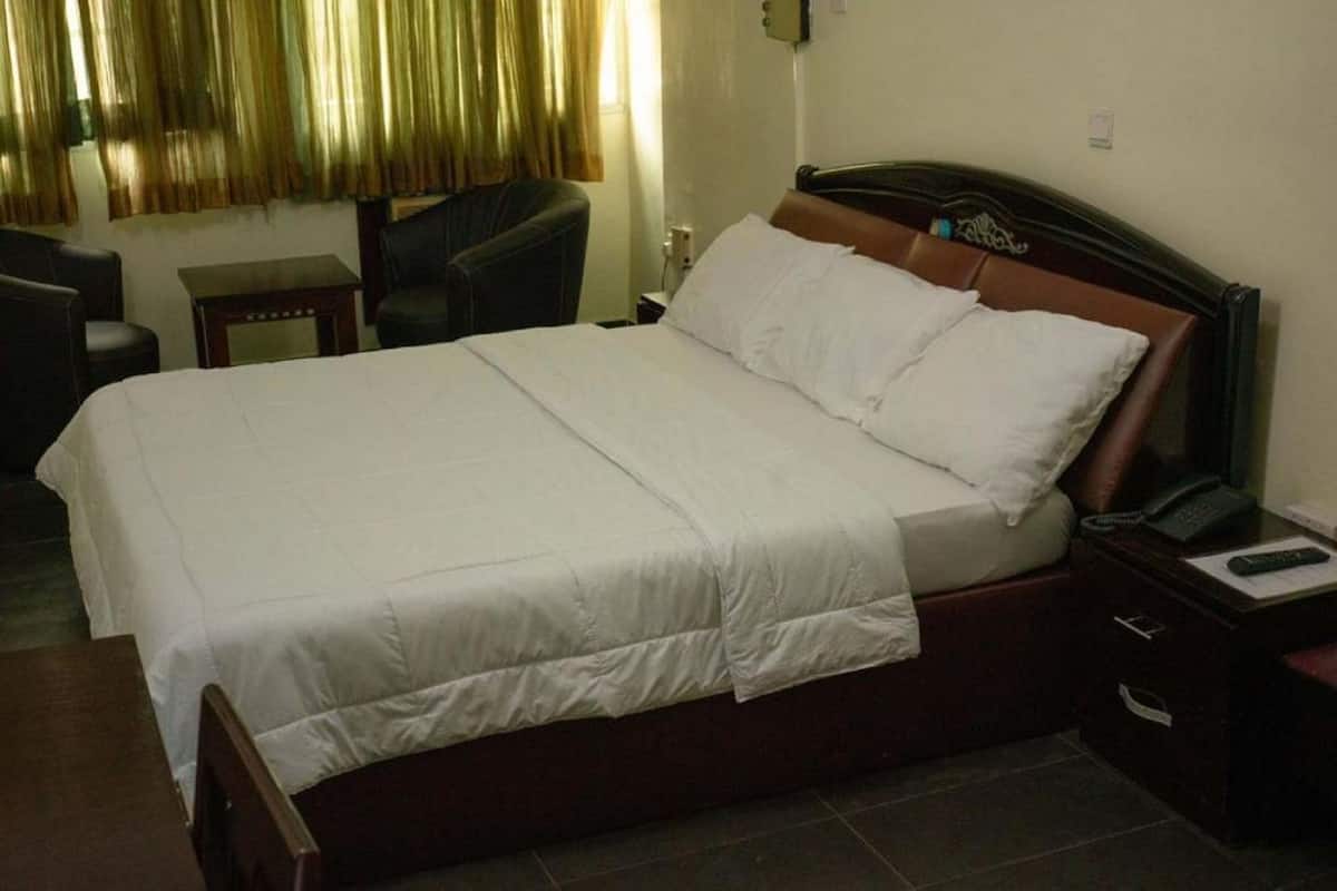 Una habitación de hotel con una cama grande, una mesita de noche con teléfono y control remoto, una silla y una pequeña mesa.