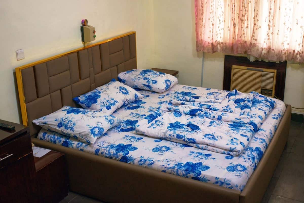Una cama con cubrecama floral, cabecera de madera y mesita de noche con lámpara.