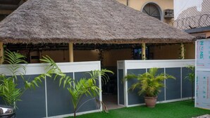 A thatched-roof structure with a white wall and green artificial grass. - Biggie Hotel and Suites  (Lagos)