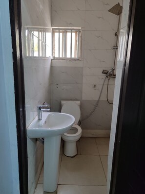 A small bathroom with a white sink, toilet, and shower. - All Saints House (Abuja)