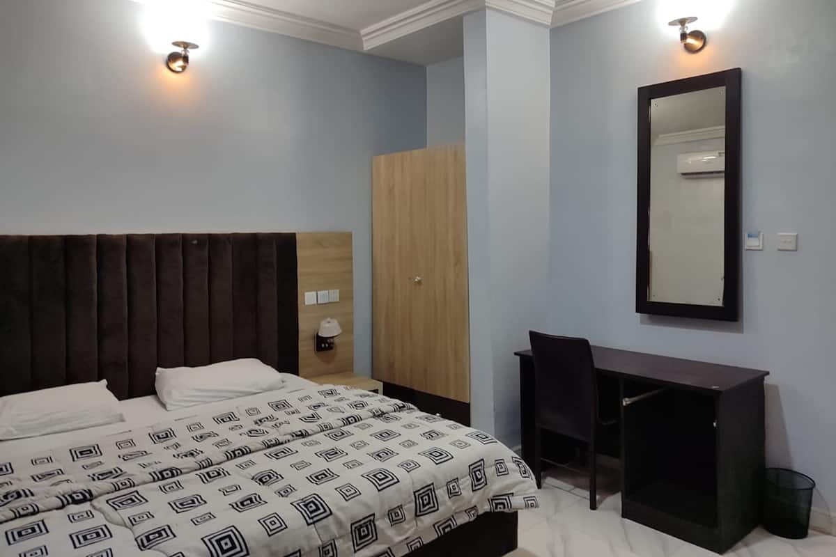 A bedroom with a bed, a desk, a chair, a wardrobe, and a mirror.