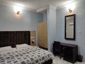 A bedroom with a bed, a desk, a chair, a wardrobe, and a mirror. - All Saints House (Abuja)